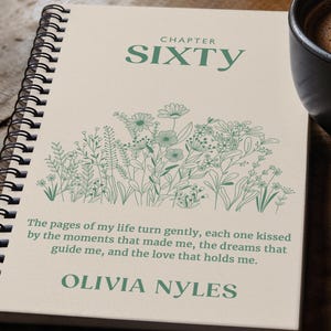 May include: A cream-coloured spiral notebook with a green floral design and the text "CHAPTER SIXTY" and "The pages of my life turn gently, each one kissed by the moments that made me, the dreams that guide me, and the love that holds me. OLIVIA NYLES".