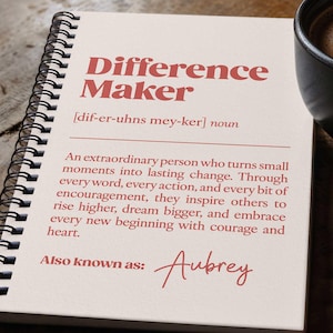 May include: A spiral-bound notebook with the words "Difference Maker" in red lettering. The definition of "Difference Maker" is printed below, along with the name "Aubrey." A black coffee mug with latte art and a pen are also visible.
