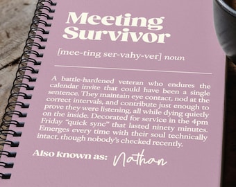 May include: A spiral-bound notebook with a dusty rose cover featuring white text that defines the term Meeting Survivor as a battle-hardened veteran who endures calendar invites, with the custom name Nathan printed at the bottom.