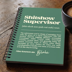 Könnte beinhalten: Ein grünes Spiralnotizbuch mit den Worten "Shitshow Supervisor" in großen, fetten Buchstaben. Das Notizbuch enthält eine Definition und den Namen "Blake" in Kursivschrift. Rechts steht eine Tasse Kaffee.