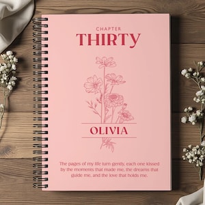 Puede incluir: Un cuaderno rosa con espiral con el texto "CHAPTER THIRTY" y el nombre "OLIVIA". Una ilustración floral está debajo del texto. La parte inferior del cuaderno tiene una cita. El cuaderno está sobre una superficie de madera.