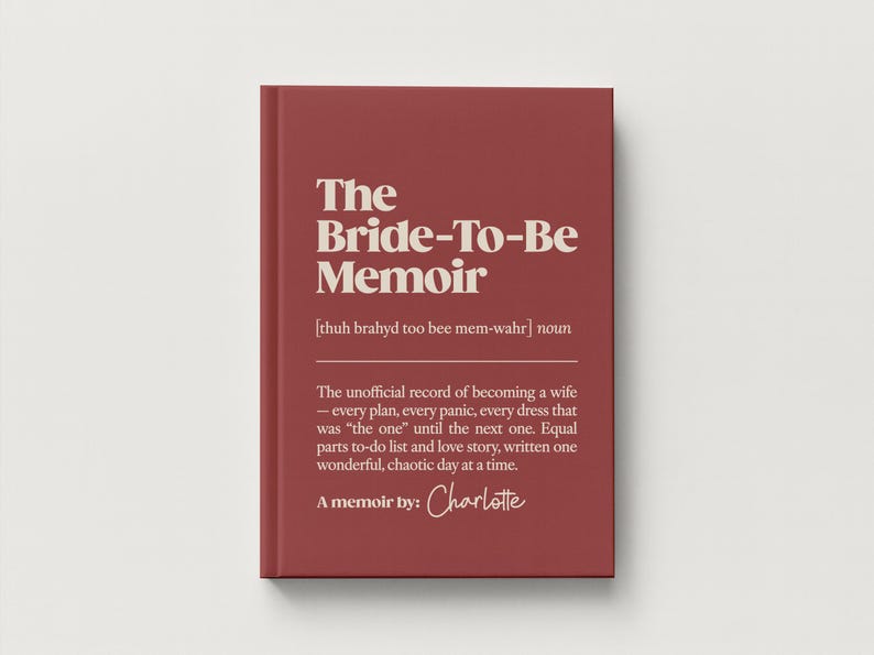 May include: A dark red hardcover book titled The Bride-To-Be Memoir in cream-colored serif font. The cover includes a phonetic pronunciation guide, the noun classification, and a descriptive paragraph about wedding planning, signed by Charlotte.