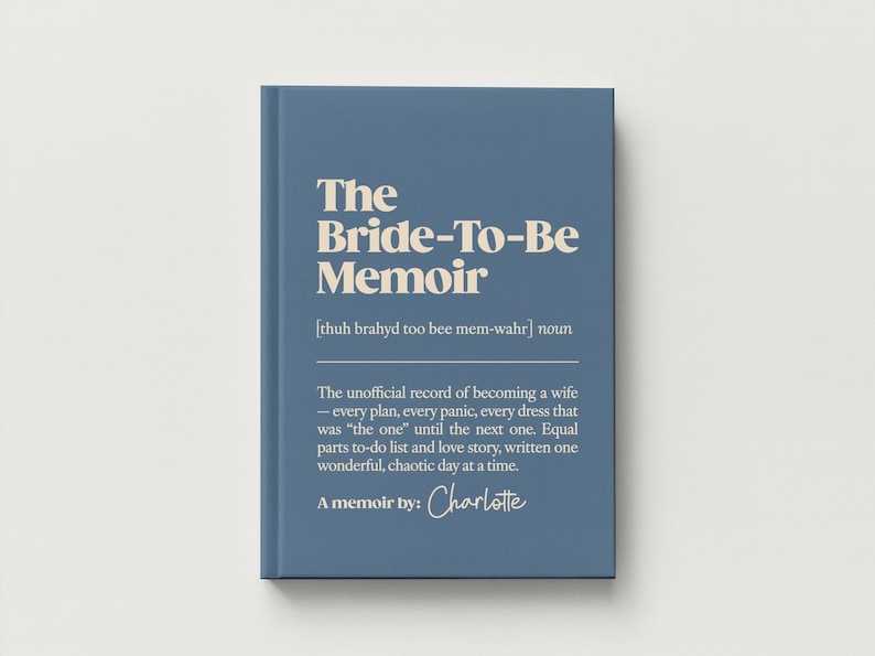 May include: A blue hardcover book titled The Bride-To-Be Memoir with cream-colored text. The cover features a phonetic pronunciation guide, a definition of the title, and the text A memoir by: Charlotte in a script font at the bottom.