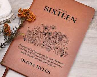 Puede incluir: Un diario de cuero marrón con las palabras "Capítulo Dieciséis" y un diseño floral. El diario está personalizado con el nombre "Olivia Nyles" y una cita sobre el viaje de la vida.