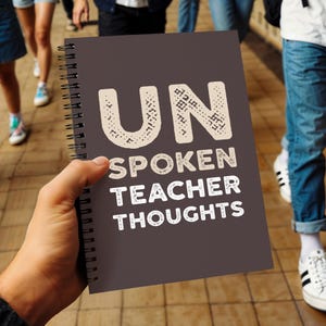 May include: A dark gray spiral-bound notebook with the words "UNSPOKEN TEACHER THOUGHTS" in white. The word "UN" is in a decorative font. The notebook is held in a person's hand.