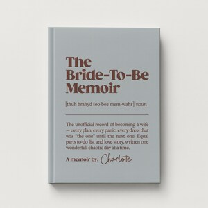 May include: A light gray hardcover book titled The Bride-To-Be Memoir in dark brown text. The cover includes a phonetic pronunciation, the noun classification, and a descriptive paragraph about wedding planning, ending with A memoir by: Charlotte.
