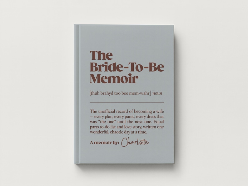 May include: A light gray hardcover book titled The Bride-To-Be Memoir in dark brown text. The cover includes a phonetic pronunciation, the noun classification, and a descriptive paragraph about wedding planning, ending with A memoir by: Charlotte.