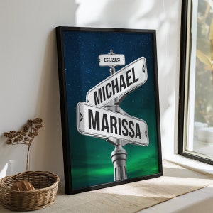May include: A framed print with a starry night sky background. Two street signs intersect, one reads "MICHAEL" and the other reads "MARISSA". The top sign also has "EST. 2023" written on it.