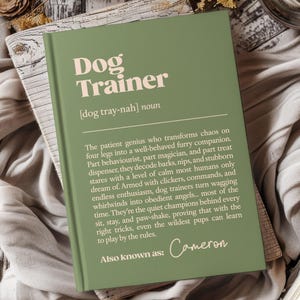 Könnte beinhalten: Ein grünes Notizbuch mit den Worten "Dog Trainer" in einer fetten, hellfarbigen Schrift. Das Notizbuch enthält eine Definition eines Hundetrainers und den Namen "Cameron" unten. Das Notizbuch liegt auf einer Holzoberfläche.