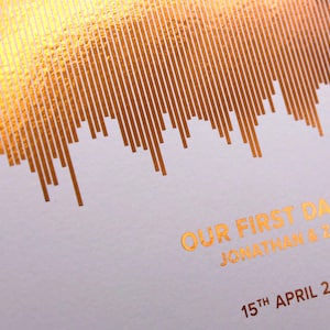 May include: A wedding keepsake with gold foil details. The design features a soundwave pattern with the text "OUR FIRST DANCE" and the names "JONATHAN & ZOE" along with the date "15TH APRIL 2023" in gold foil.