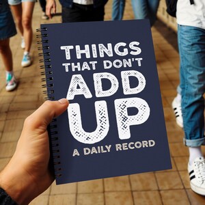 Può includere: Un taccuino a spirale blu scuro con il testo bianco "THINGS THAT DON'T ADD UP A DAILY RECORD" stampato sulla copertina anteriore. Il taccuino presenta una rilegatura a spirale in metallo nero sul lato sinistro e una finitura opaca sulla copertina.