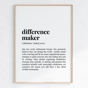 Może przedstawiać: Oprawiony wydruk z definicją "difference maker" w czarnym tekście na białym tle. Definicja opisuje entuzjastyczną osobę, która wierzy, że może zmienić świat. Rama jest w kolorze jasnego drewna.
