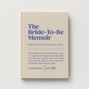 May include: A beige hardcover book titled The Bride-To-Be Memoir in blue text. The cover includes a phonetic pronunciation, the noun definition, and a description of the content as an unofficial record of becoming a wife, signed by Charlotte.
