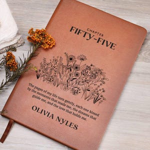 May include: A brown leather journal with the text "CHAPTER FIFTY-FIVE" and a floral design. The quote "The pages of my life turn gently, each one kissed by the moments that made me, the dreams that guide me, and the love that holds me." is engraved on the cover, along with the name "OLIVIA NYLES".