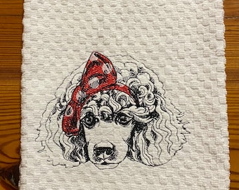 May include: White kitchen towel with an embroidered image of a poodle wearing a red bow. The poodle is facing forward with its head tilted slightly to the side.