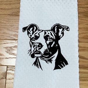 May include: White hand towel with a black and white illustration of a dog's face. The dog has large, floppy ears and a focused expression. The towel is made of a textured fabric.