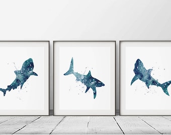 May include: Set of three watercolor shark prints in shades of blue and green. Each print features a stylized shark silhouette with a splatter effect.