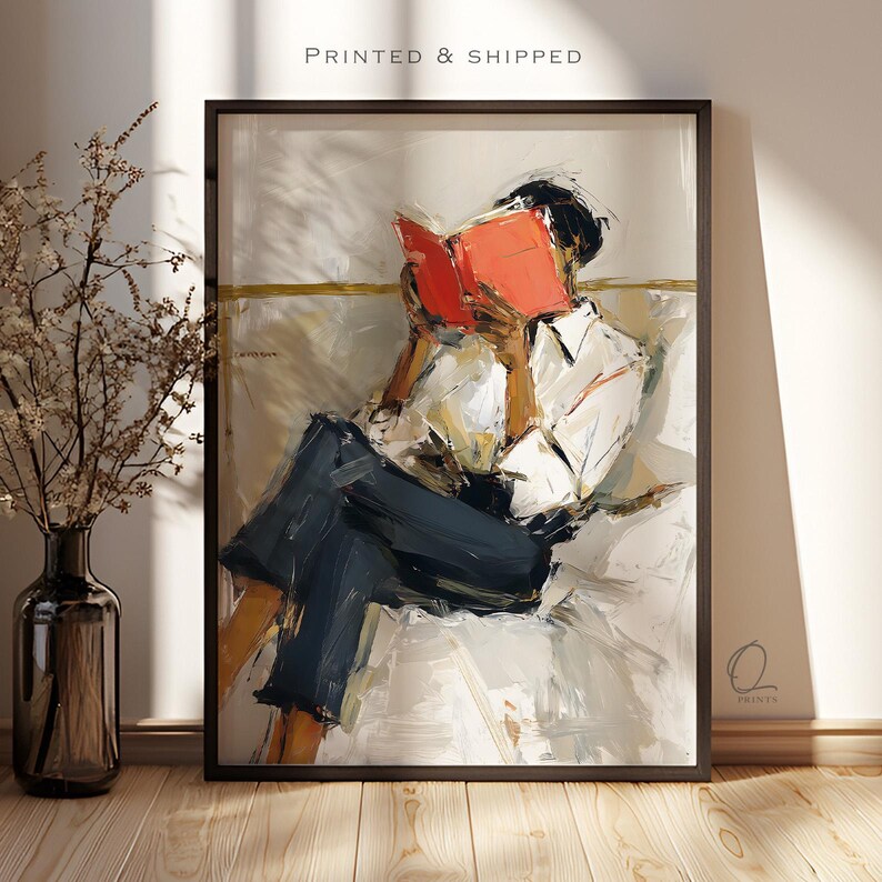 May include: Abstract art print of a person reading a book. The person is wearing a white shirt and dark blue pants. The book is open, with bright orange pages. The artwork is framed in a black frame. The text "PRINTED & SHIPPED" is at the top.