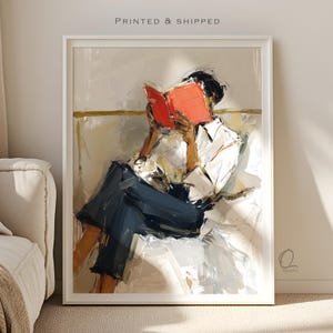 May include: Abstract art print of a person reading a book. The person is wearing a white shirt and dark blue pants, seated on a white couch. The book is bright red. The print is in a white frame. The text "PRINTED & SHIPPED" is at the top.