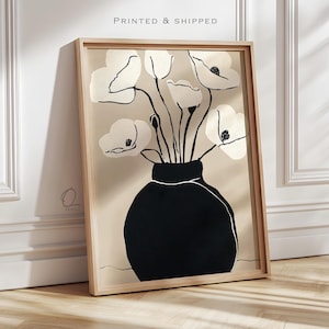 May include: A framed wall art print featuring a black vase holding white flowers with black outlines against a beige background. The text PRINTED & SHIPPED appears at the top, and a small logo with the letter Q and the word PRINTS is visible.
