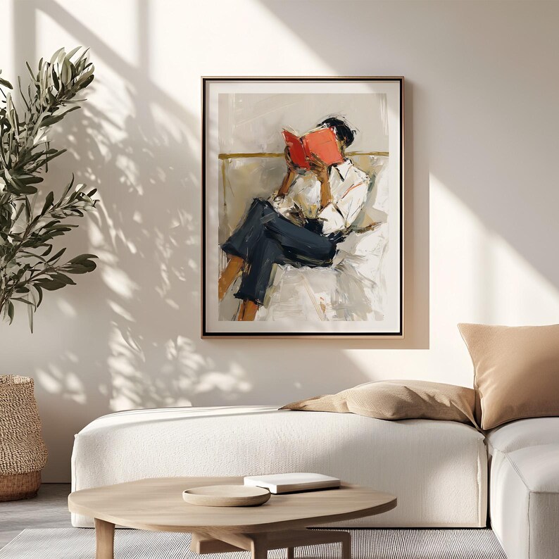 May include: Framed art print featuring an abstract painting of a person reading a book. The person is wearing a white shirt and dark blue pants. The book is bright red, and the artwork has a neutral color palette with a gold frame.