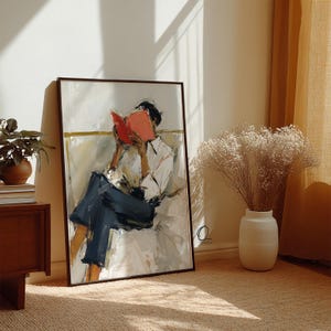 May include: A framed art print depicts a person reading a book. The artwork features a person in a white shirt and dark blue pants, with a red book. The painting has a neutral color palette with a brown frame.