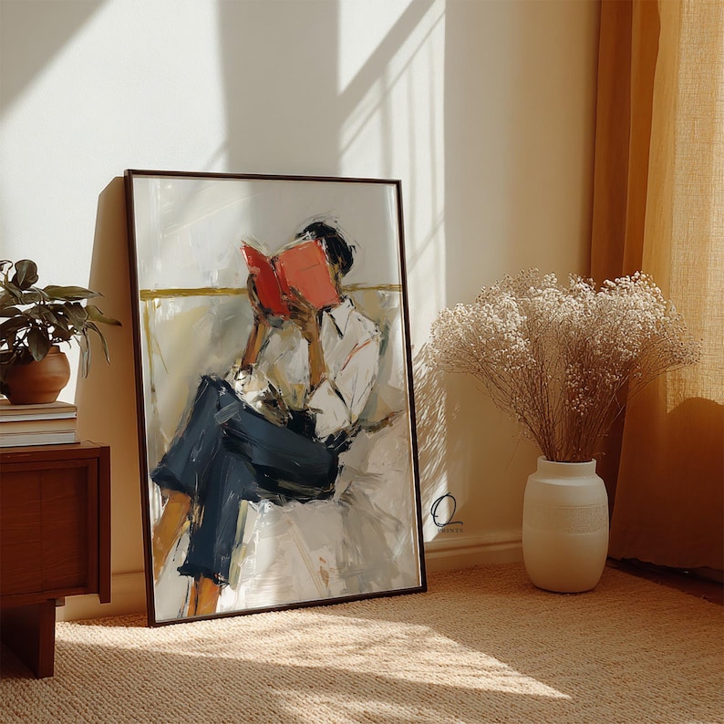 May include: A framed art print depicts a person reading a book. The artwork features a person in a white shirt and dark blue pants, with a red book. The painting has a neutral color palette with a brown frame.