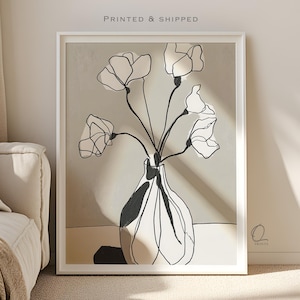 May include: A framed art print with a minimalist floral design. The artwork shows a vase with black and white flowers. The print has a neutral colour palette with the text "PRINTED & SHIPPED" at the top. The artist's signature is in the bottom right corner.