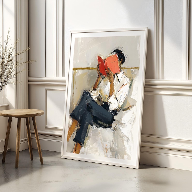 May include: An abstract painting in a white frame depicts a person reading a book. The person is wearing a white shirt and dark blue pants. The book is bright red, and the background is neutral tones.