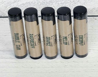 Op de afbeelding: Vijf bruine lippenbalsem tubes met zwarte dopjes. De tubes zijn gelabeld met de smaken: kokosnoot, meloen, sinaasappel, framboos en bubblegum.