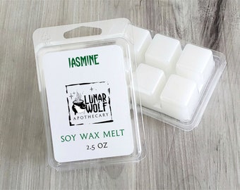 Puede incluir: Un paquete de plástico transparente que contiene seis cubos de cera de soja blanca. El paquete tiene una etiqueta que dice "Jasmine" y "Soy Wax Melt 2.5 oz" con un logotipo en blanco y negro que dice "Lunar Wolf Apothecary".