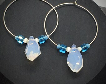 Puede incluir: Un par de pendientes de aro de plata con una piedra de ópalo azul claro en forma de lágrima que cuelga de cada aro. Los aros están adornados con pequeñas cuentas azules y blancas.