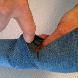 May include: A close-up of a blue fabric being stretched and pulled by a hand. The fabric has a textured, knitted appearance.