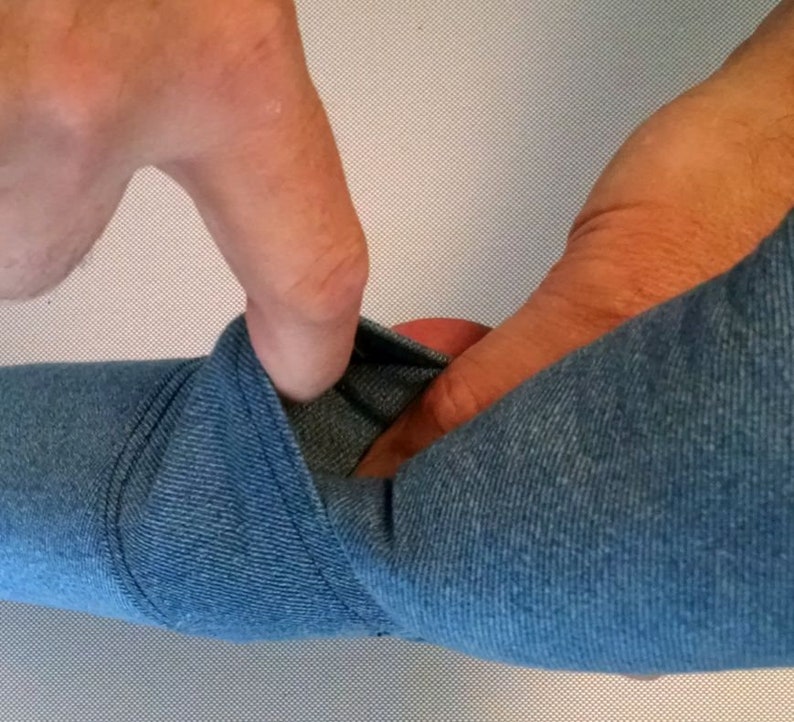 May include: A close-up of a blue fabric being stretched and pulled by a hand. The fabric has a textured, knitted appearance.
