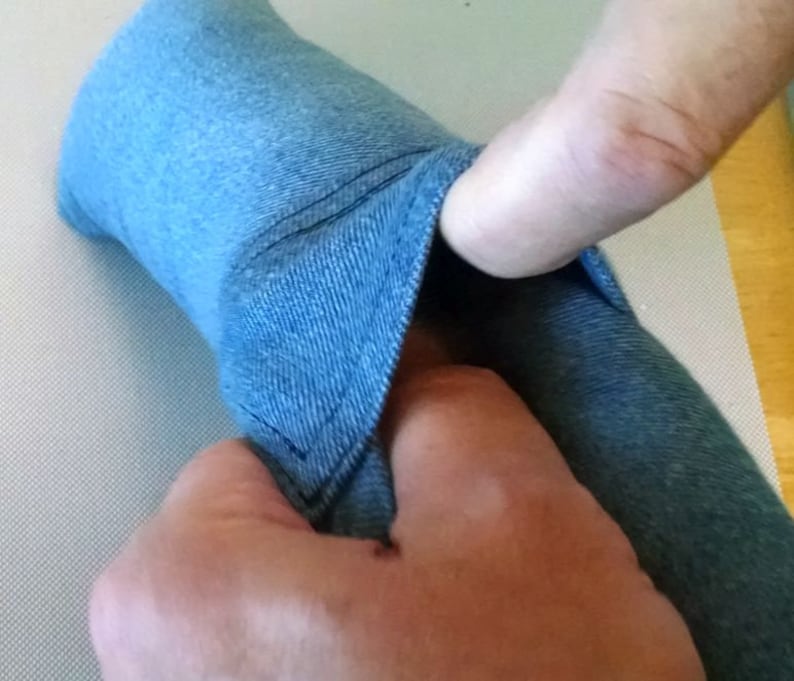 May include: A close-up of a blue denim fabric being pulled apart to reveal the inside of the fabric. The fabric is soft and has a subtle texture.