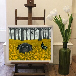 May include: A framed print of a black and white illustration of a creature with large eyes and a wide smile, surrounded by yellow flowers. A blue butterfly is flying above the creature. The print is on an easel in front of a white wall.