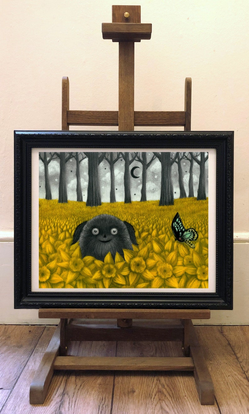 May include: A framed illustration of a black furry creature with large eyes, sitting in a field of yellow daffodils. A blue butterfly flies above the creature. The background is a dark forest with a crescent moon in the sky.