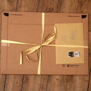 May include: A brown cardboard package tied with a yellow ribbon. The package has a handwritten note that says "Thank you". The package also has a sticker that says "Climate neutral".