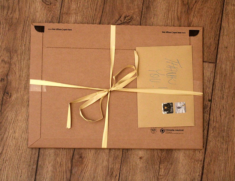 May include: A brown cardboard package tied with a yellow ribbon. The package has a handwritten note that says "Thank you". The package also has a sticker that says "Climate neutral".
