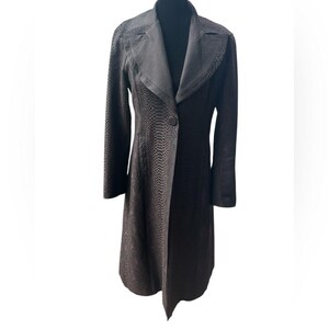 May include: A dark brown, long coat with a textured, snakeskin-like pattern. The coat has a notched lapel, a single-button closure, and long sleeves. The coat is displayed on a black mannequin.