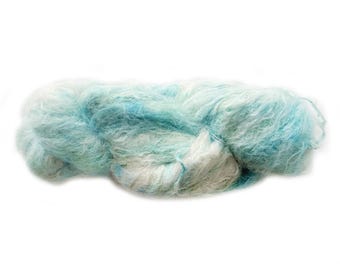 Puede incluir: Una madeja de hilo suave y difuso que presenta una mezcla variada de fibras blancas, azul pálido y turquesa. La textura es ligera y aireada con un efecto halo distintivo, creando una apariencia similar a una nube en todo el hilo retorcido.