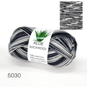 May include: A skein of black, white, and gray yarn labeled "ALOE SOCKWOOL" with the composition 75% wool and 25% polyamid. The label also states 100g = ca. 420m and 30m = 10cm. The yarn is wound into a ball shape.