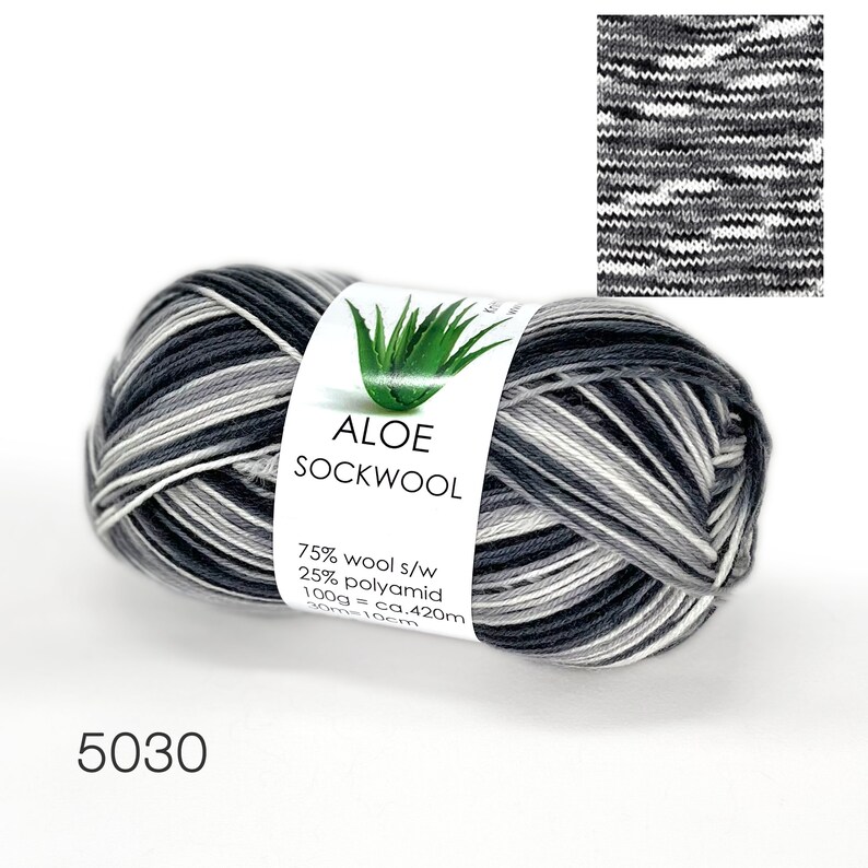 May include: A skein of black, white, and gray yarn labeled "ALOE SOCKWOOL" with the composition 75% wool and 25% polyamid. The label also states 100g = ca. 420m and 30m = 10cm. The yarn is wound into a ball shape.