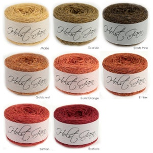 Puede incluir: Ocho ovillos de lana redondos etiquetados como Holst Garn en varios colores: Maize, Scarab, Scots Pine, Goldcrest, Burnt Orange, Ember, Saffron y Bokhara. Cada ovillo tiene una banda de papel blanca con el nombre de la marca en cursiva.