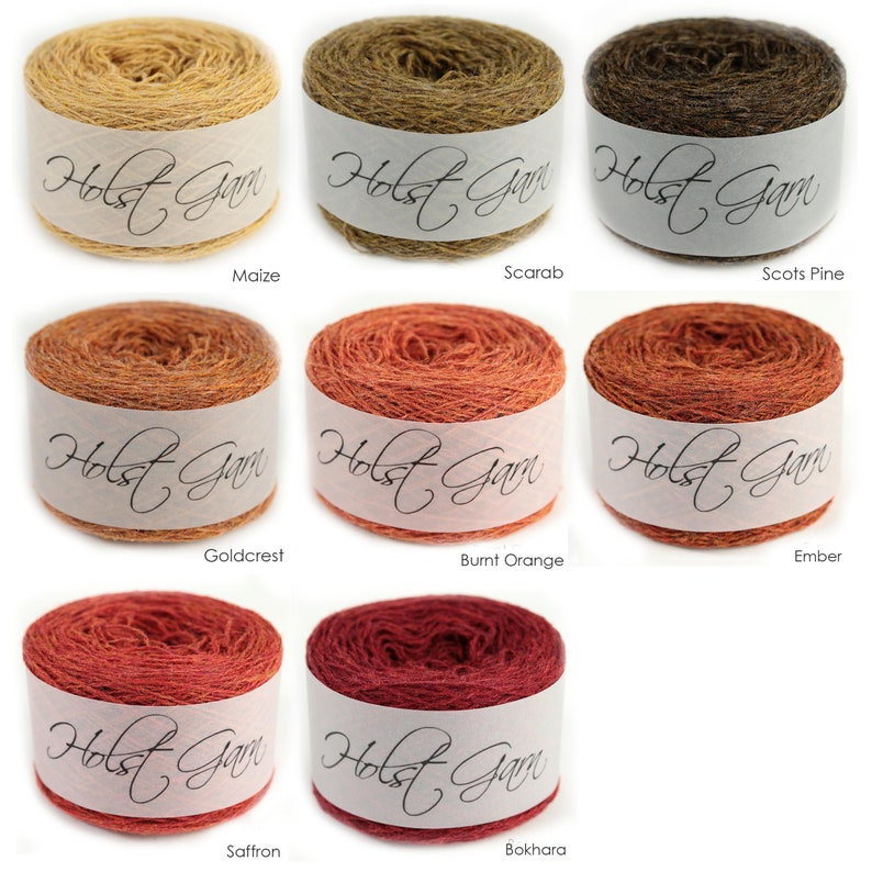 Puede incluir: Ocho ovillos de lana redondos etiquetados como Holst Garn en varios colores: Maize, Scarab, Scots Pine, Goldcrest, Burnt Orange, Ember, Saffron y Bokhara. Cada ovillo tiene una banda de papel blanca con el nombre de la marca en cursiva.