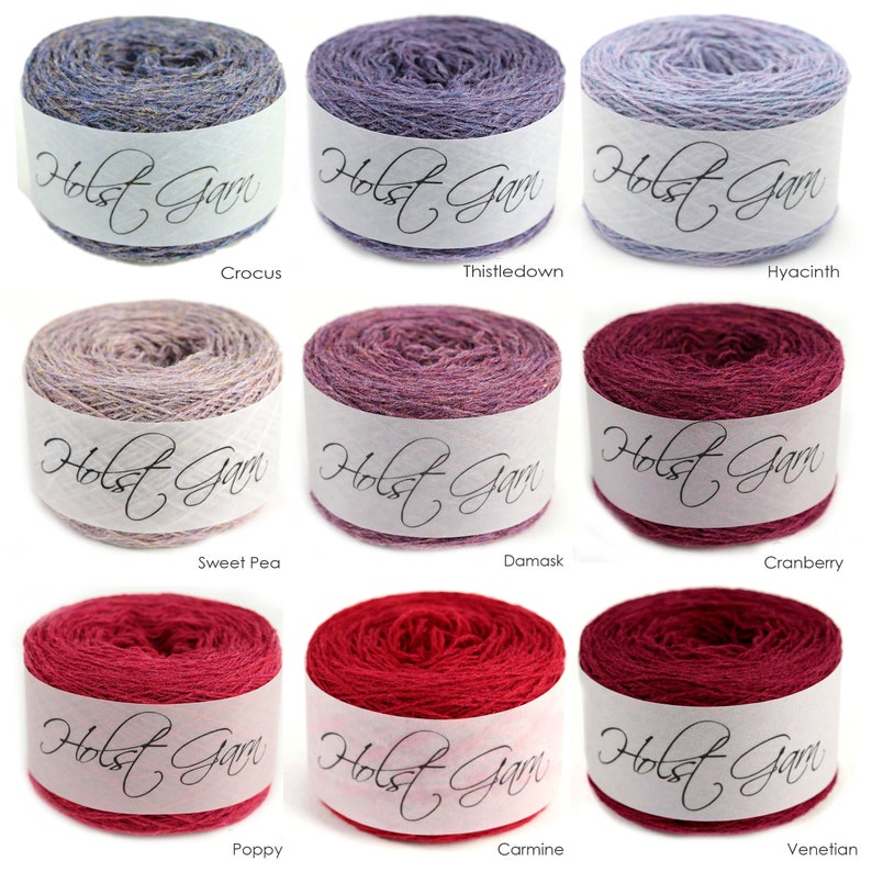 Puede incluir: Nueve ovillos de lana cil&iacute;ndricos dispuestos en cuadr&iacute;cula, cada uno envuelto en una banda de papel blanco con la etiqueta Holst Garn. Los colores incluyen tonos de azul, morado, lavanda, beige, rosa, magenta y rojo oscuro, etiquetados como Crocus, Thistledown, Hyacinth, Sweet Pea, Damask, Cranberry, Poppy, Carmine y Venetian.
