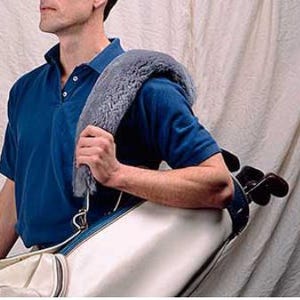 May include: A gray, plush shoulder pad attached to a white and blue golf bag. The pad is designed to cushion the shoulder while carrying the bag. The bag contains several golf clubs.