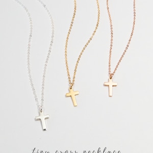 May include: Three delicate gold, silver, and rose gold necklaces with tiny cross pendants. The necklaces are on a white background with the text "tiny cross necklace BY MONDAY MONARCH".