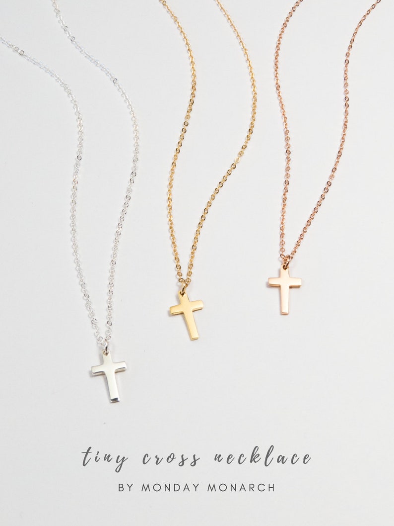 May include: Three delicate gold, silver, and rose gold necklaces with tiny cross pendants. The necklaces are on a white background with the text "tiny cross necklace BY MONDAY MONARCH".