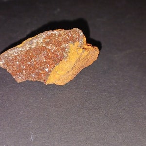 May include: A rough, irregularly shaped rock with a reddish-brown color and a layer of sparkly, light brown crystals.